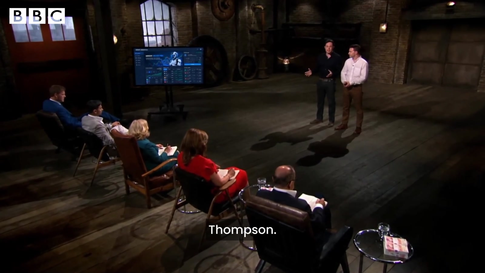The Dragons' Den with two founders and five dragons seated, a Smart Investing dashboard on screen